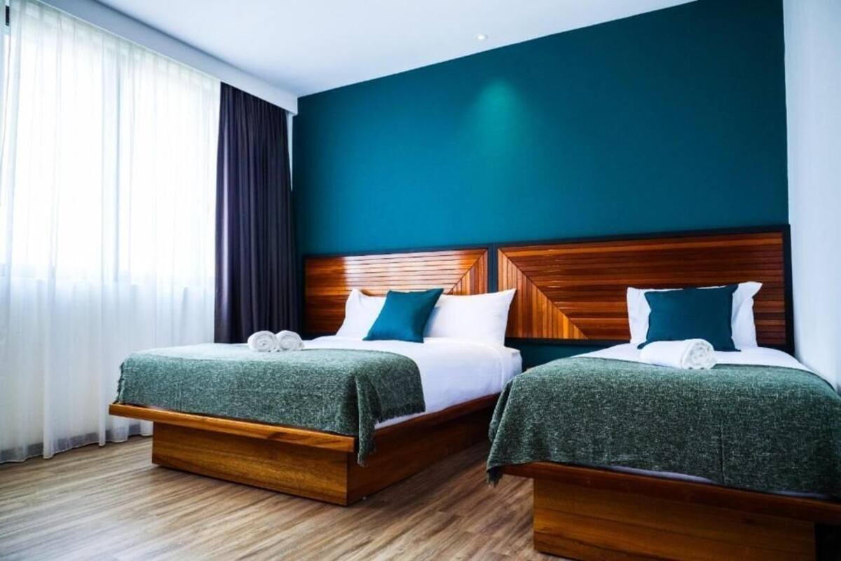 Habitación de hotel con dos camas, cabeceros de madera y un gran ventanal con cortinas.