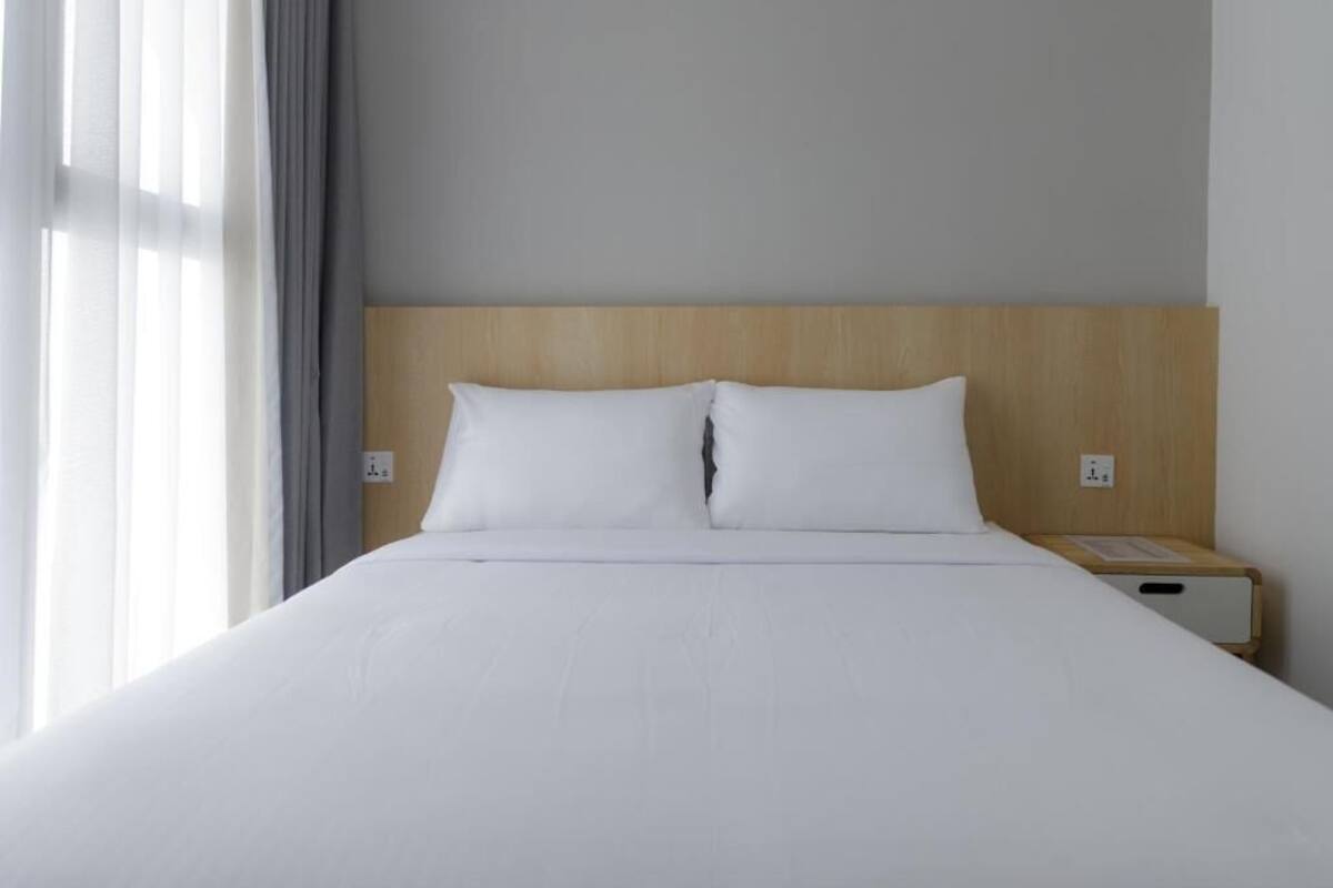 Una habitación de hotel con una cama grande, cabecera de madera, mesita de noche y ventana con cortinas.