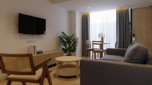 A modern living room with a flat-screen TV, a wooden dining table, a sofa, and a potted plant. - The Journey Hotel Penang (George Town)
