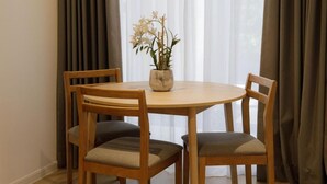 A round wooden table with two chairs, a vase with flowers, and sheer curtains. - The Journey Hotel Penang (George Town)