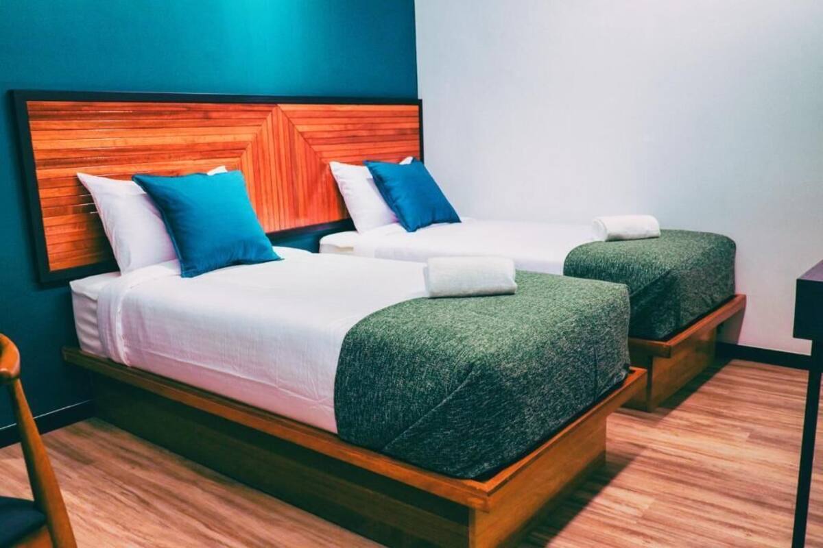 Habitación de hotel con dos camas individuales, cada una con cabecero de madera, ropa de cama blanca y mantas decorativas verdes.