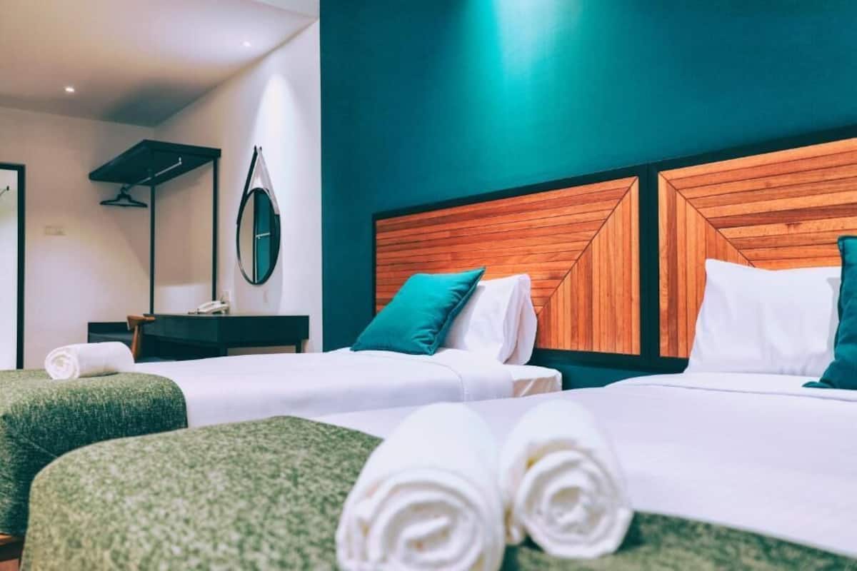 Habitación de hotel con dos camas, un cabecero de madera, un espejo y un pequeño escritorio con teléfono.