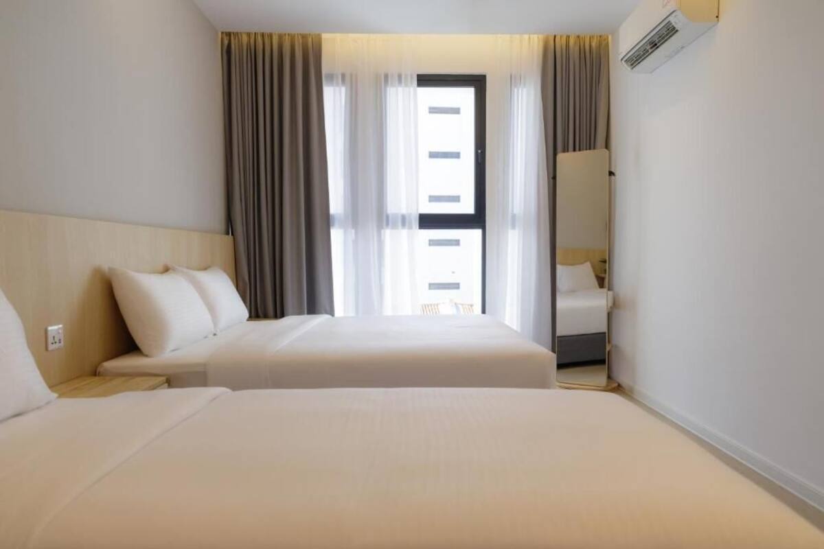 Una habitación de hotel con dos camas, una ventana con cortinas, un espejo y un equipo de aire acondicionado.