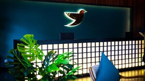 A reception desk with a logo, a plant, and a blue pillow. - The Journey Hotel Penang (George Town)