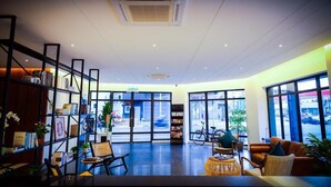 A modern interior with a reception desk, seating area, and large windows offering a view of the street. - The Journey Hotel Penang (George Town)