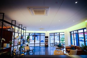 A modern interior with a reception desk, seating area, and large windows offering a view of the street. - The Journey Hotel Penang (George Town)