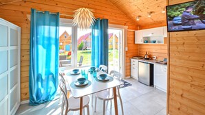 Um quarto aconchegante em estilo cabana, com uma mesa de jantar posta para quatro pessoas, uma área de cozinha com lava-louças e uma TV fixada na parede.