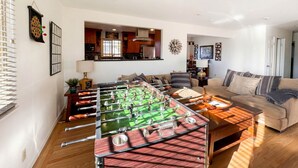 Una sala de estar con mesa de fútbol, un sofá y una cocina al fondo.