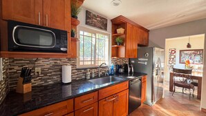 Una cocina moderna con armarios de madera, un microondas negro, un refrigerador de acero inoxidable y un ventanal que proporciona luz natural.