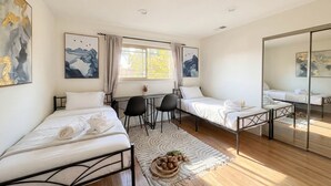 Un dormitorio moderno con dos camas individuales, un escritorio, sillas y un espejo grande.