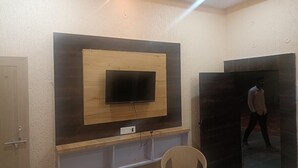 Una sala de estar moderna con un televisor de pantalla plana grande montado en una pared de madera, una silla de mimbre y una puerta que da a otra habitación.