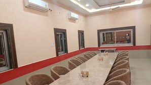 Un salón de conferencias con una larga mesa, sillas, unidades de aire acondicionado y una ventana con vistas.