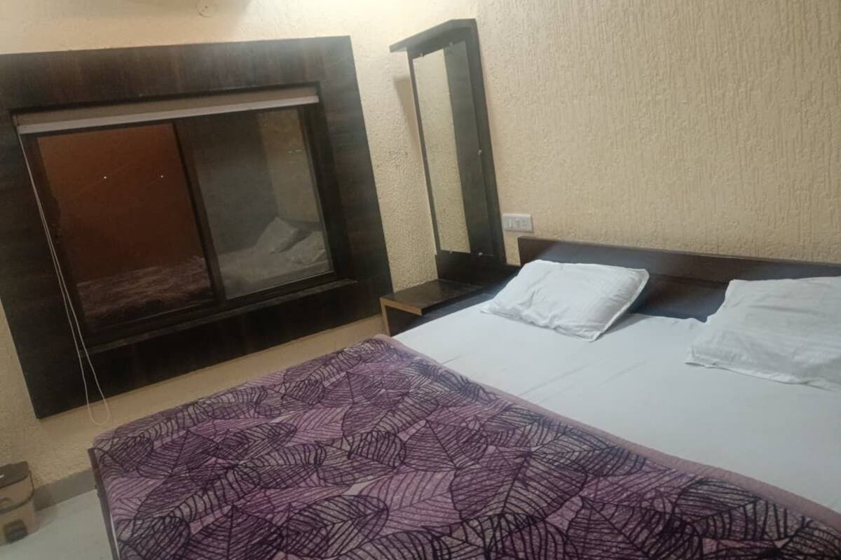 A hotel room with a bed, a headboard, a bedside table, and a wall-mounted air conditioner.