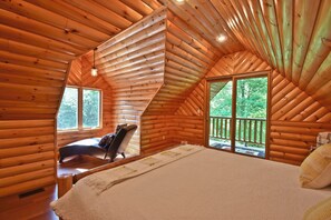 Ein Schlafzimmer in einer Blockhütte mit einem Bett, einem Sessel und einem Fenster mit Blick auf einen Balkon.