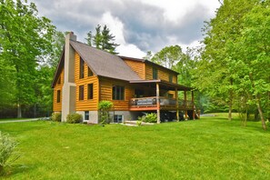 Eine Blockhütte mit Veranda, umgeben von einem gepflegten Rasen und Bäumen.