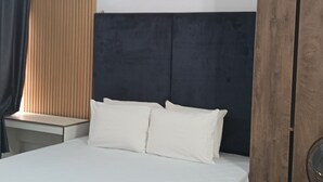 A bedroom with a bed, a nightstand, a wooden headboard, and a window with blinds. - Kbazzapartments (Ibadan)