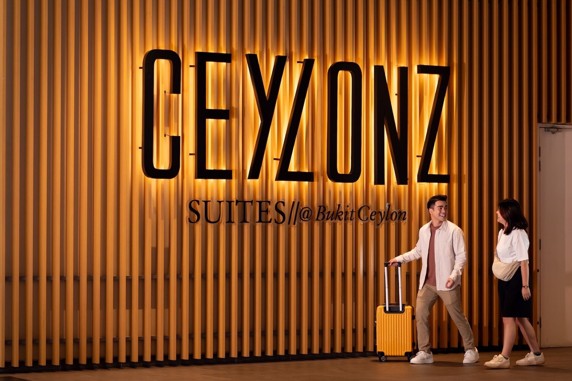 A hotel interior with a large sign reading "CEYZONZ SUITES" and a man pulling a suitcase.