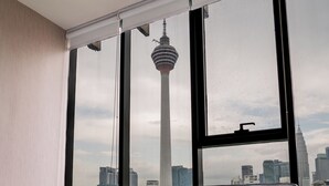 Ein modernes Zimmer mit grauem Sofa, einem Bett mit weißer Bettwäsche und großen Fenstern mit Blick auf die Stadt.