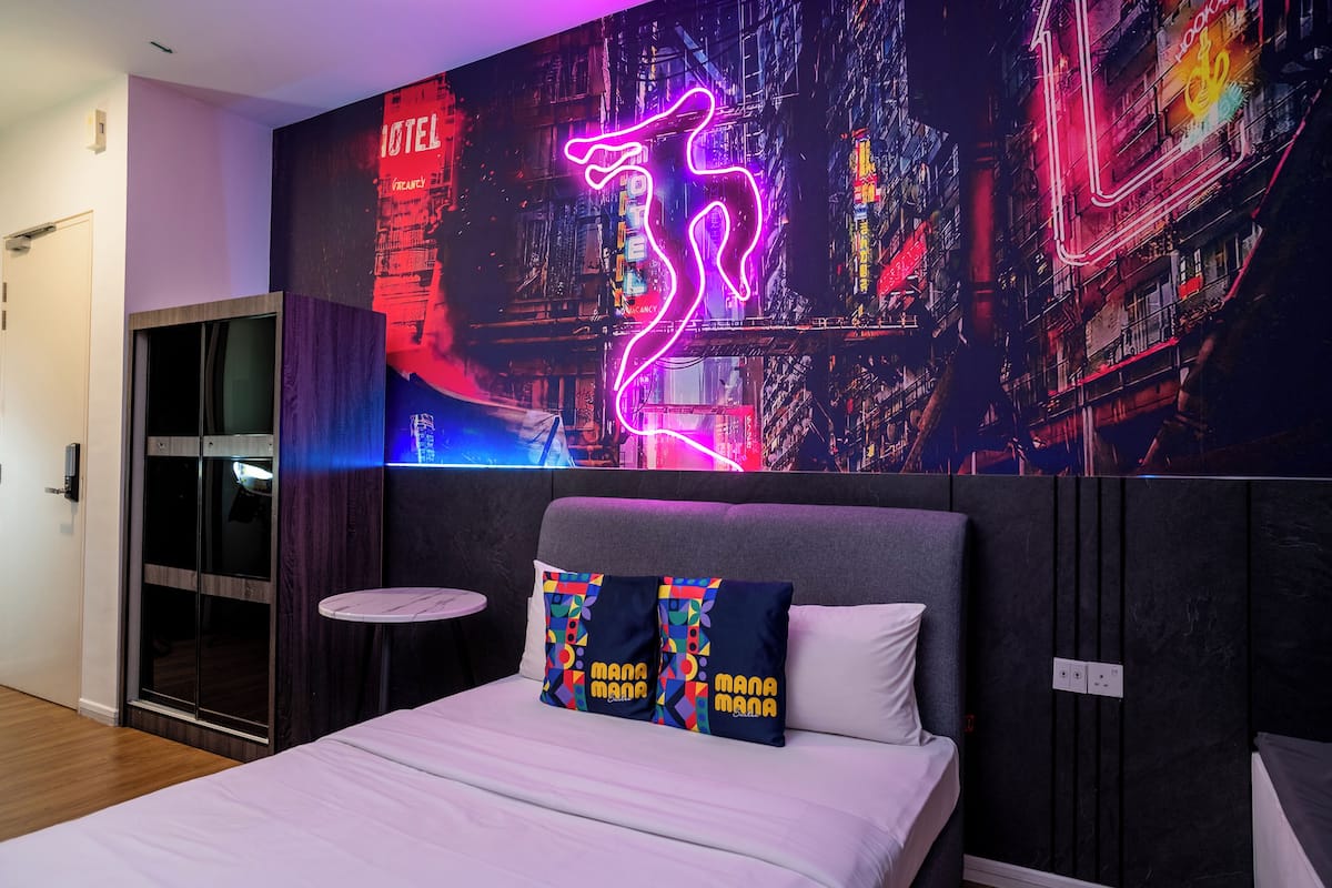 Una habitación de hotel moderna con una cama, un letrero de neón y un mural de un paisaje urbano en la pared.