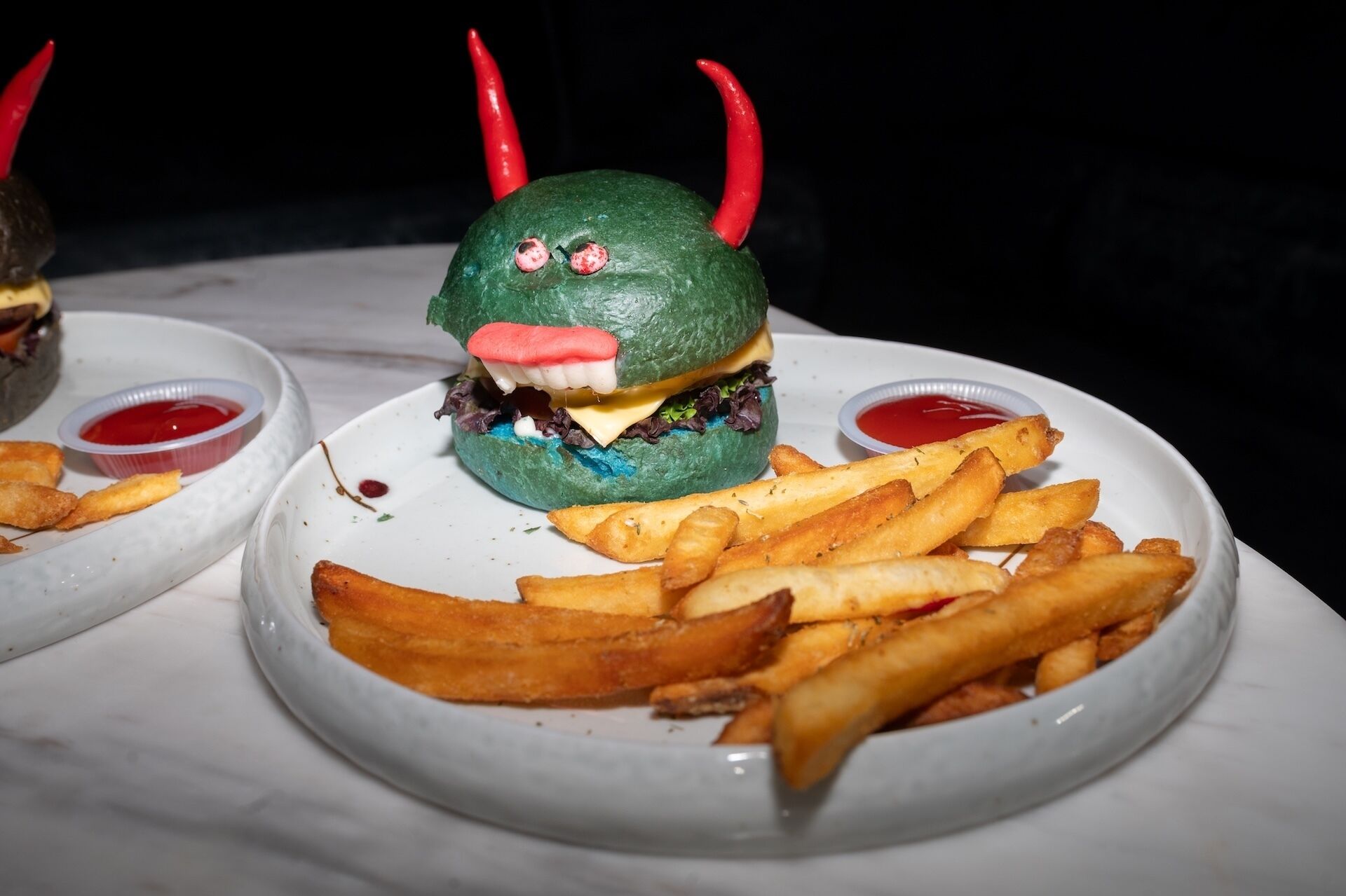A burger with a green exterior and red horns, served with fries and ketchup.
