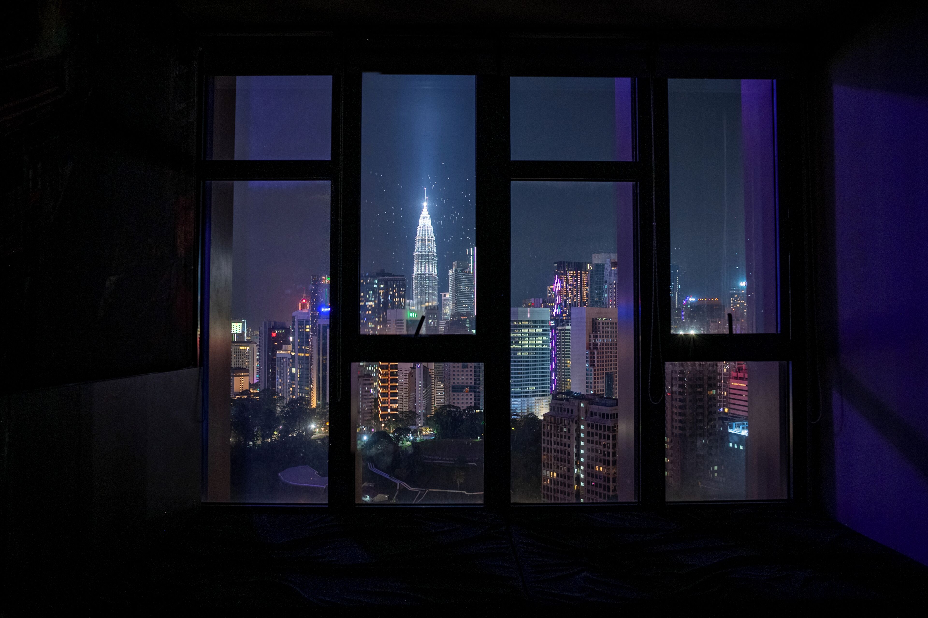 A window with a view of a cityscape at night, including a prominent building with lights.