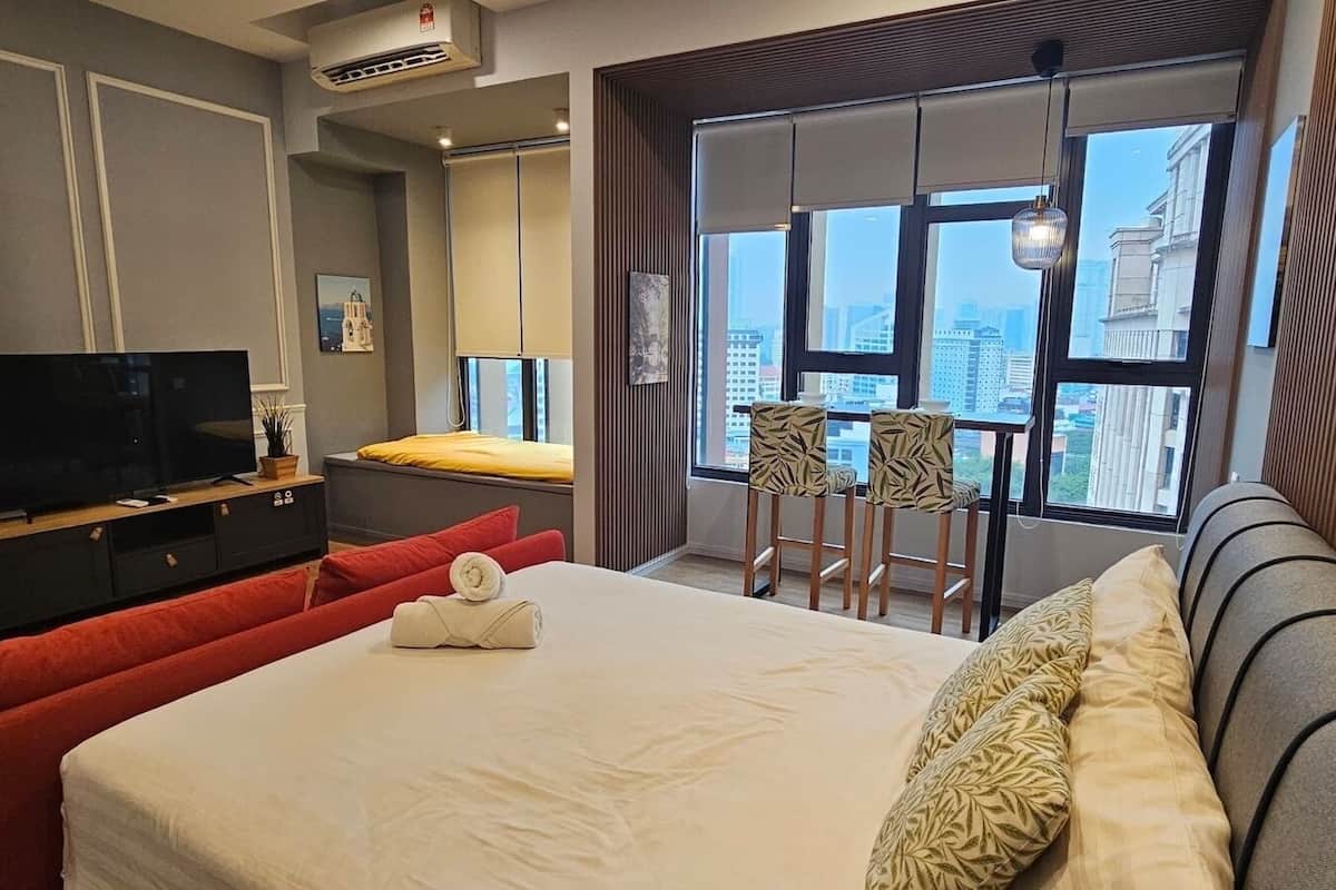 Habitación de hotel con cama, televisión, balcón con sillas y vista a la ciudad.