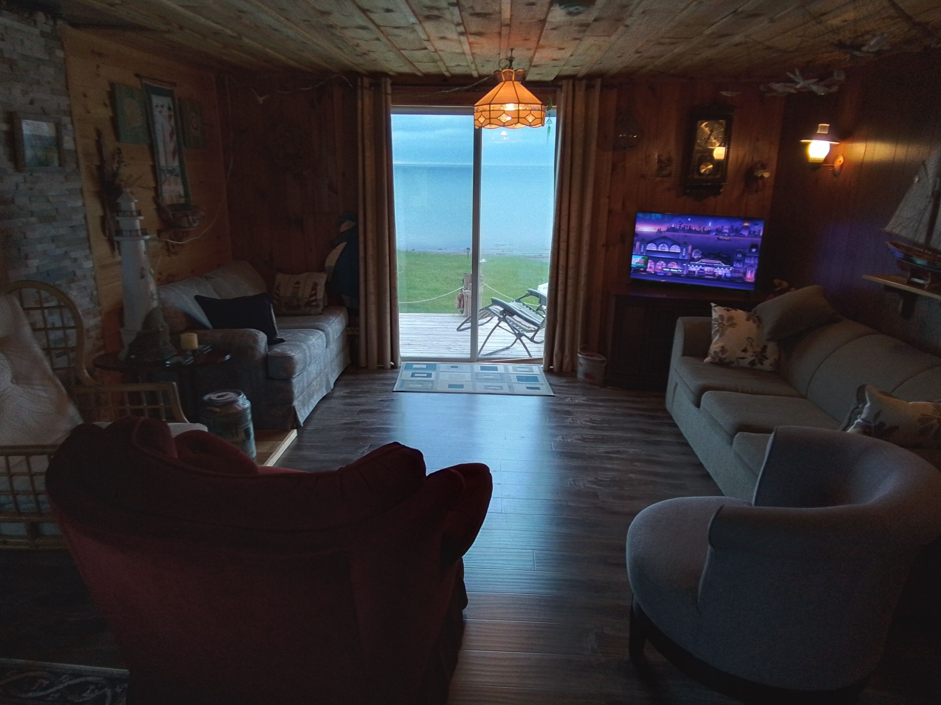 Un salon chaleureux avec un plancher en bois, un canapé, un fauteuil rouge et un téléviseur.