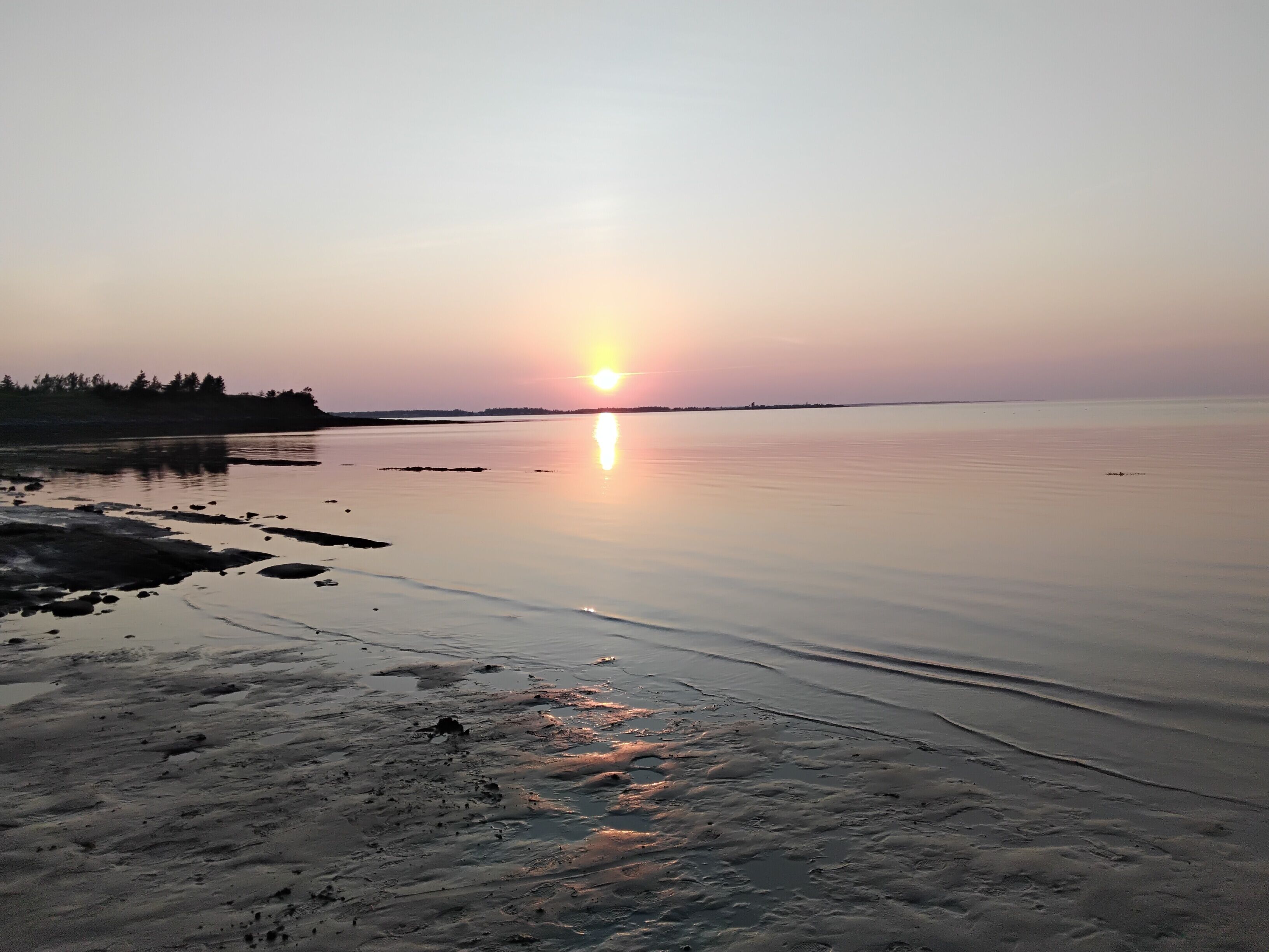 Une étendue d'eau calme où se reflète le soleil, avec une rive lointaine et un ciel dégagé.
