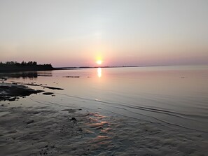 Un cuerpo de agua tranquila que refleja el sol, con una costa distante y un cielo despejado.