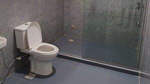 Ένα σύγχρονο μπάνιο με ένα ντους που διαχωρίζεται με γυάλινο διάφραγμα, μια τουαλέτα και ένα παράθυρο με περσίδες.