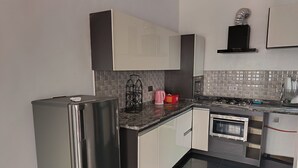 Μια σύγχρονη κουζίνα με συσκευές από ανοξείδωτο ατσάλι, λευκά ντουλάπια και πλακάκια στον τοίχο πάνω από τον πάγκο.