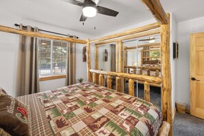 Een slaapkamer met een bed, een plafondventilator, een raam met gordijnen en een houten leuning.
