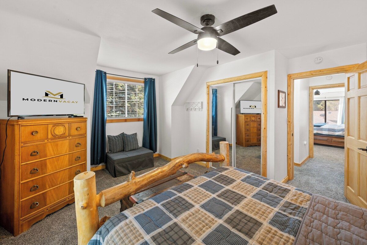 Un dormitorio con cama, cómoda de madera, ventilador de techo y televisor.