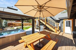 Een houten terras met een jacuzzi, picknicktafel en parasol.