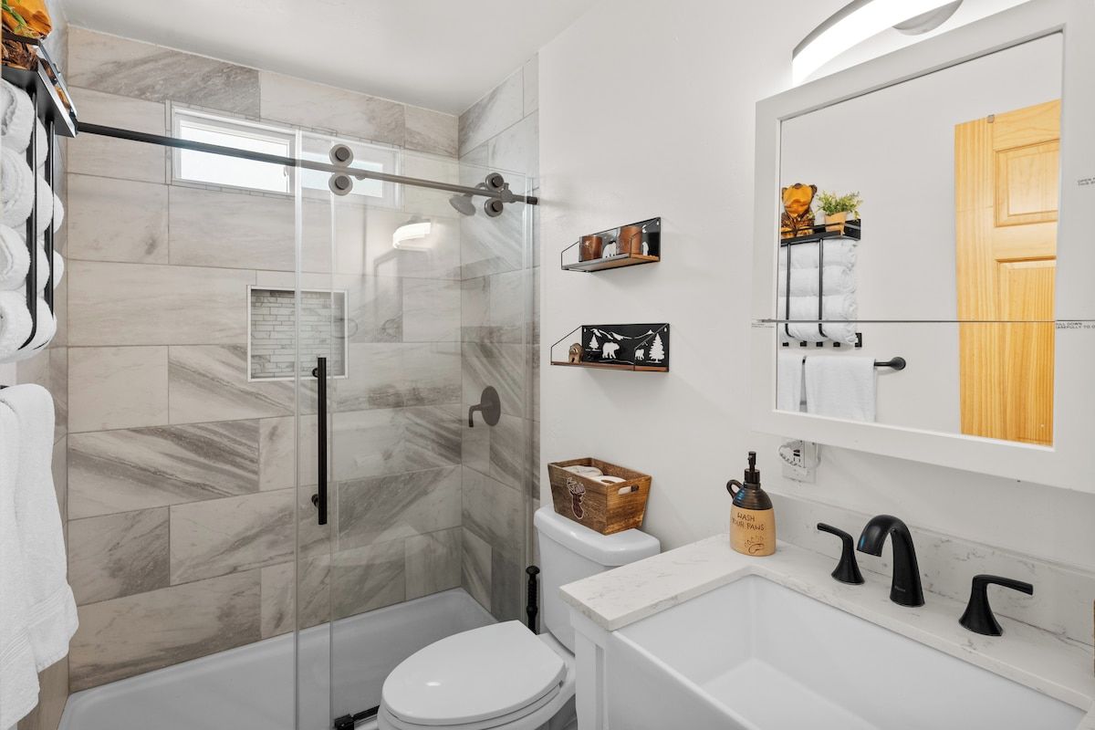 A modern bathroom with a glass-enclosed shower, a white toilet, and a sink with black faucets.