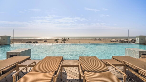 Ein Pool mit Liegestühlen, Blick auf den Strand und einem Rettungsturm.