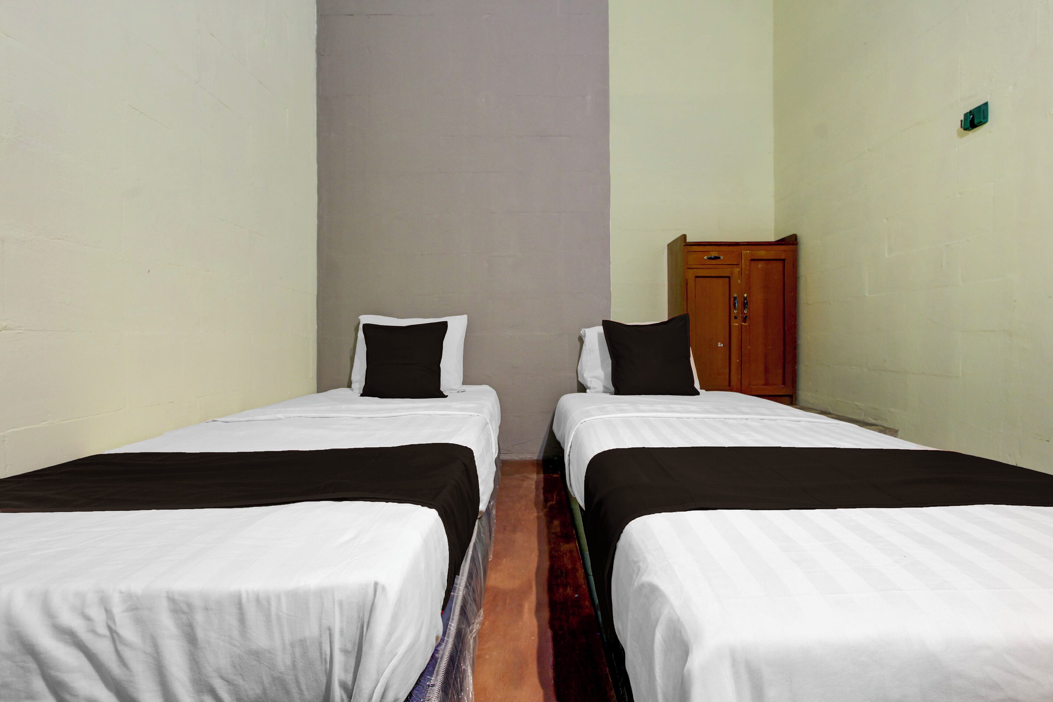 Una habitación con dos camas individuales, cada una con cabecera negra y ropa de cama blanca, y un armario de madera adosado a la pared.