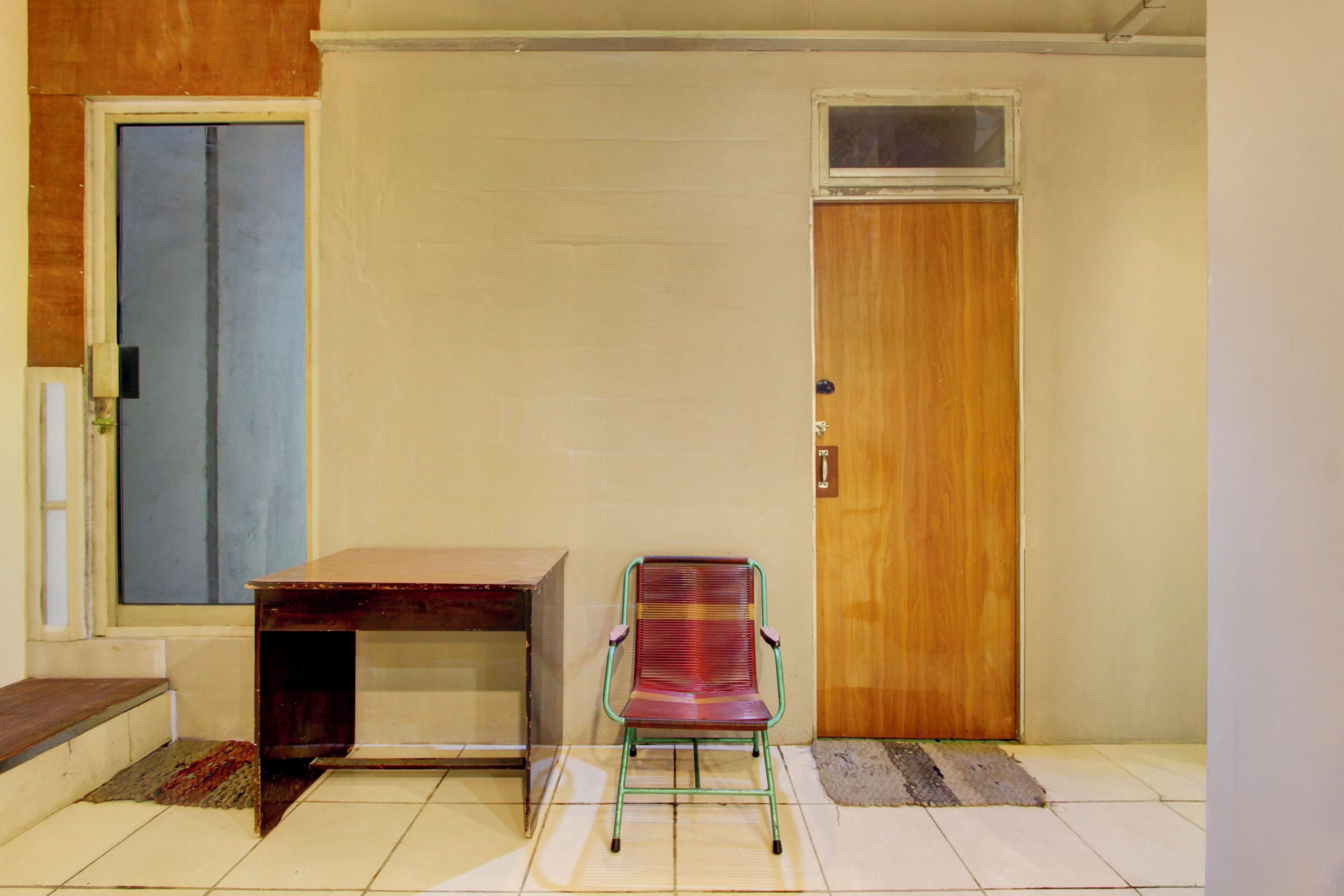 Una habitación con puerta de madera, ventana, una mesita y una silla.