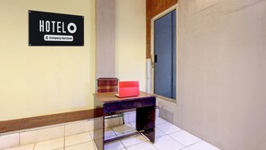 Interior de hotel com aviso indicando serviço corporativo, uma mesa com uma pasta vermelha e uma porta com janela.