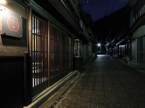 Une ruelle étroite bordée de bâtiments de style japonais traditionnel, avec une porte en bois et une enseigne portant des caractères japonais.