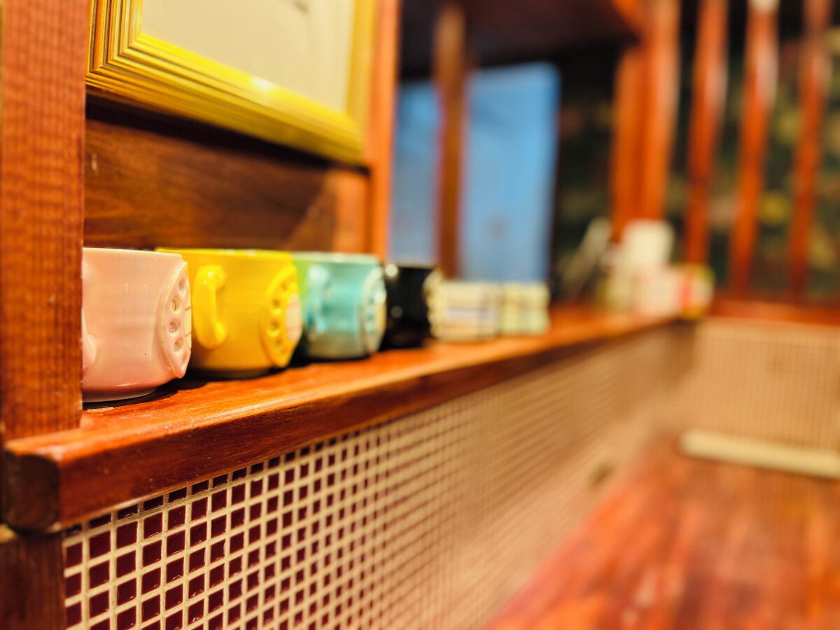 A wooden shelf with various containers, including a pink mug, a yellow container, and a blue container.