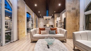Una sala de estar moderna con una mesa de centro de mármol, un conjunto de sofás y una cocina al fondo.