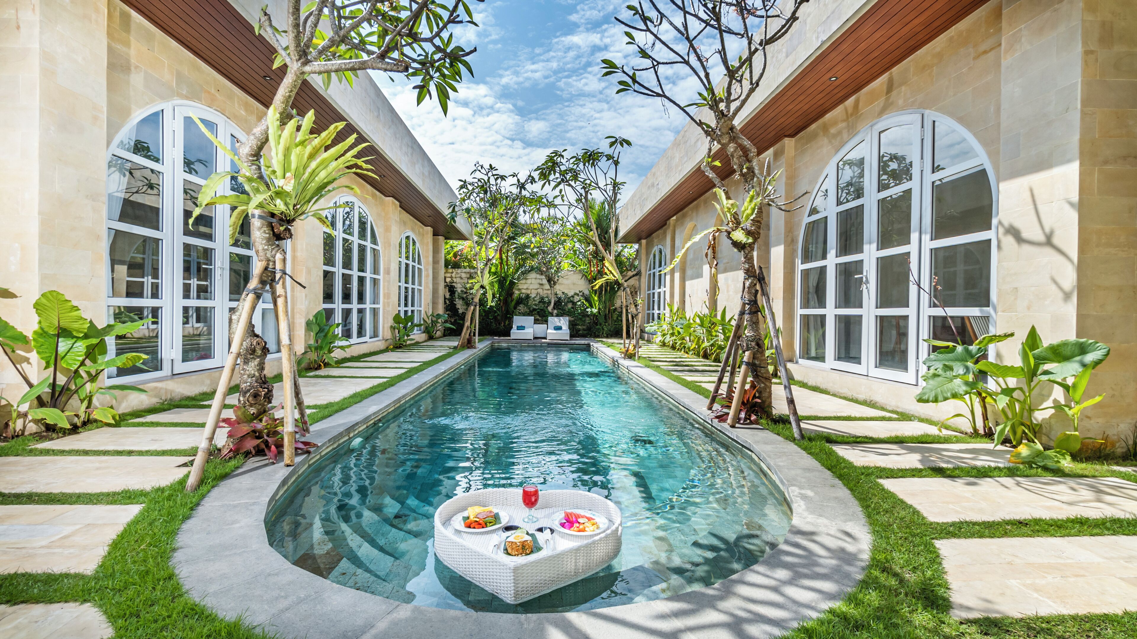 A swimming pool with a floating bar area, surrounded by lush greenery and large windows.