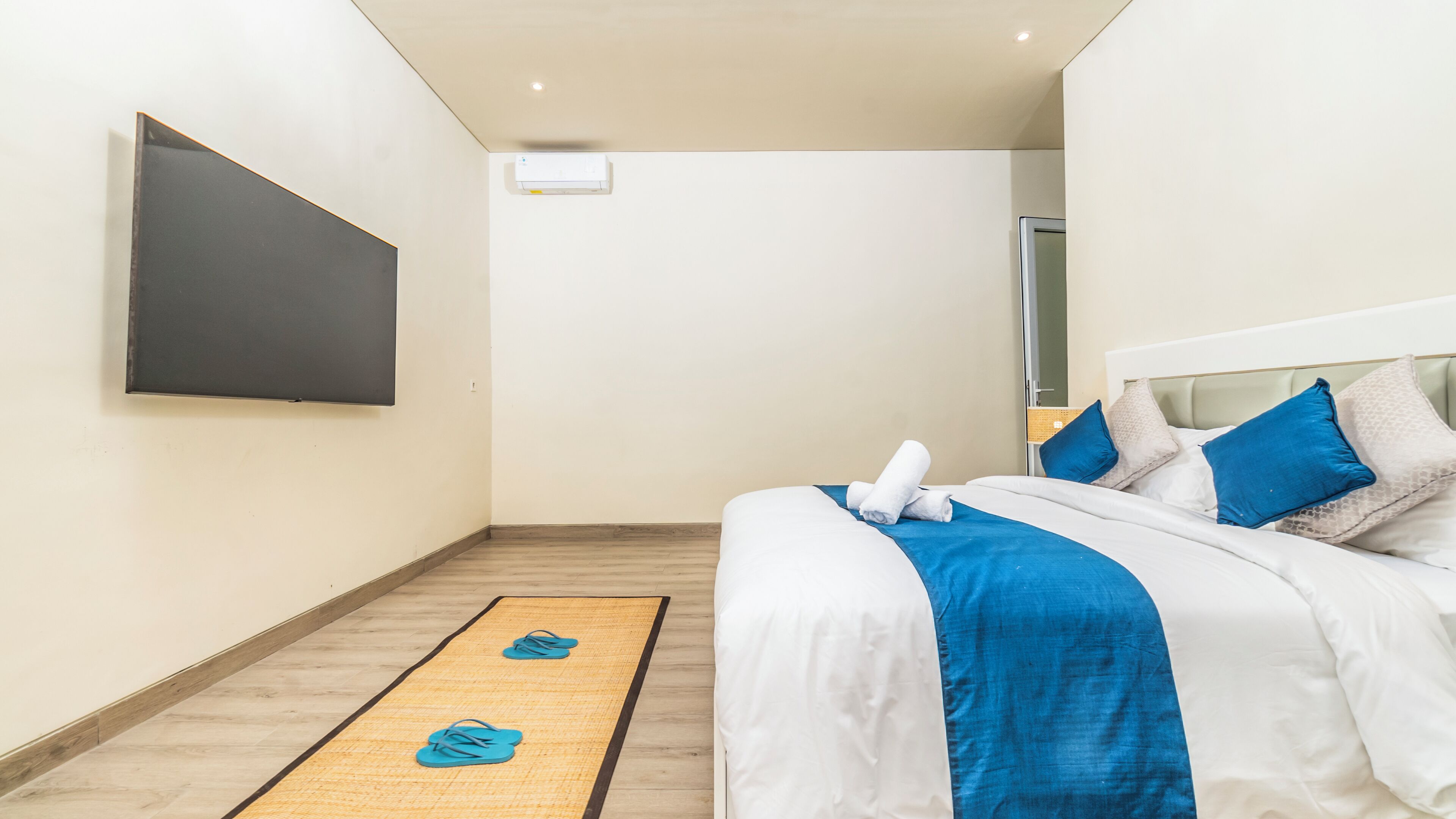 A modern hotel room with a large bed, a flat-screen TV mounted on the wall, and a wooden floor.