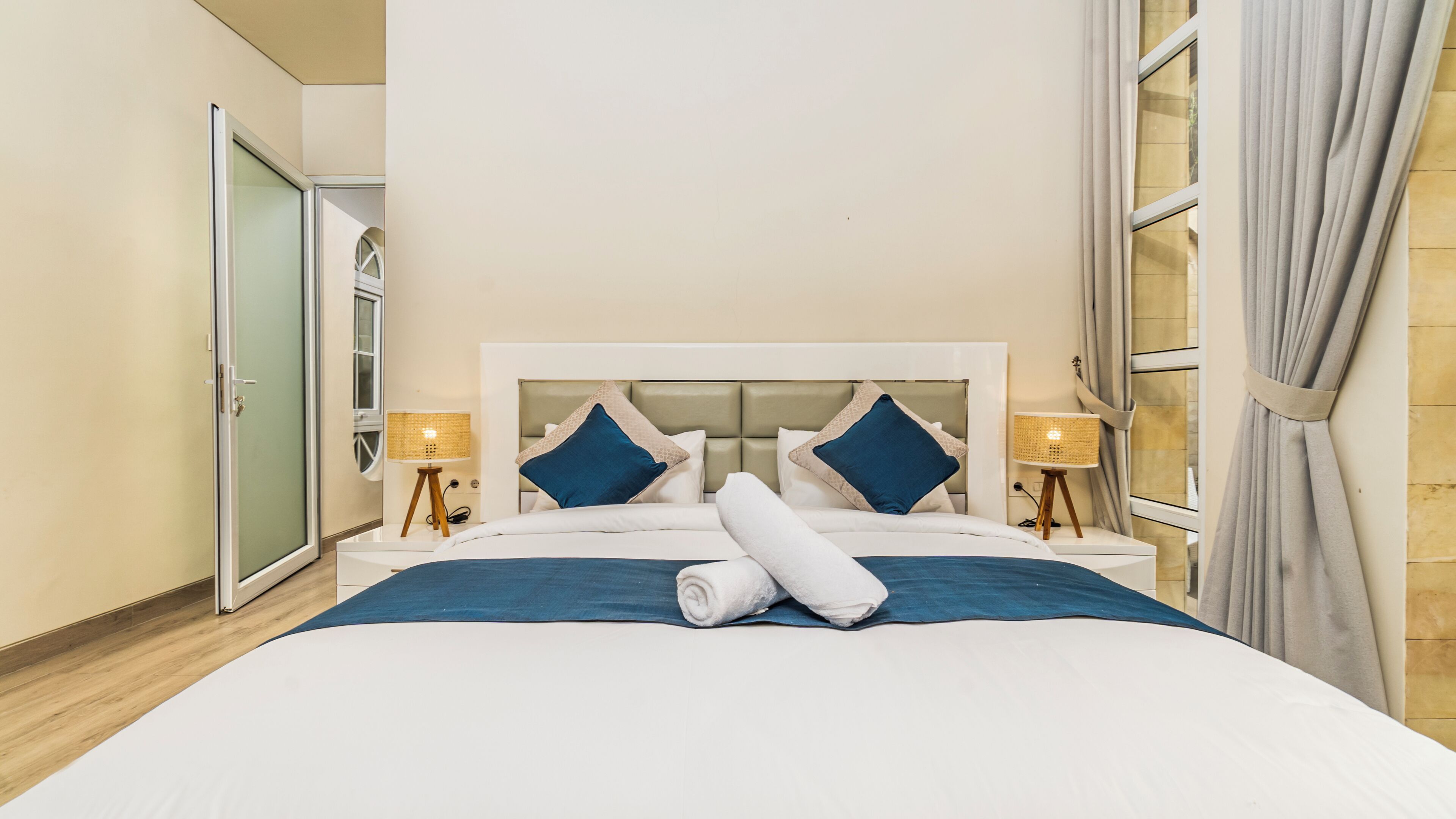 Habitación de hotel con una cama grande, dos lámparas de noche, cabecera y una ventana con cortinas.