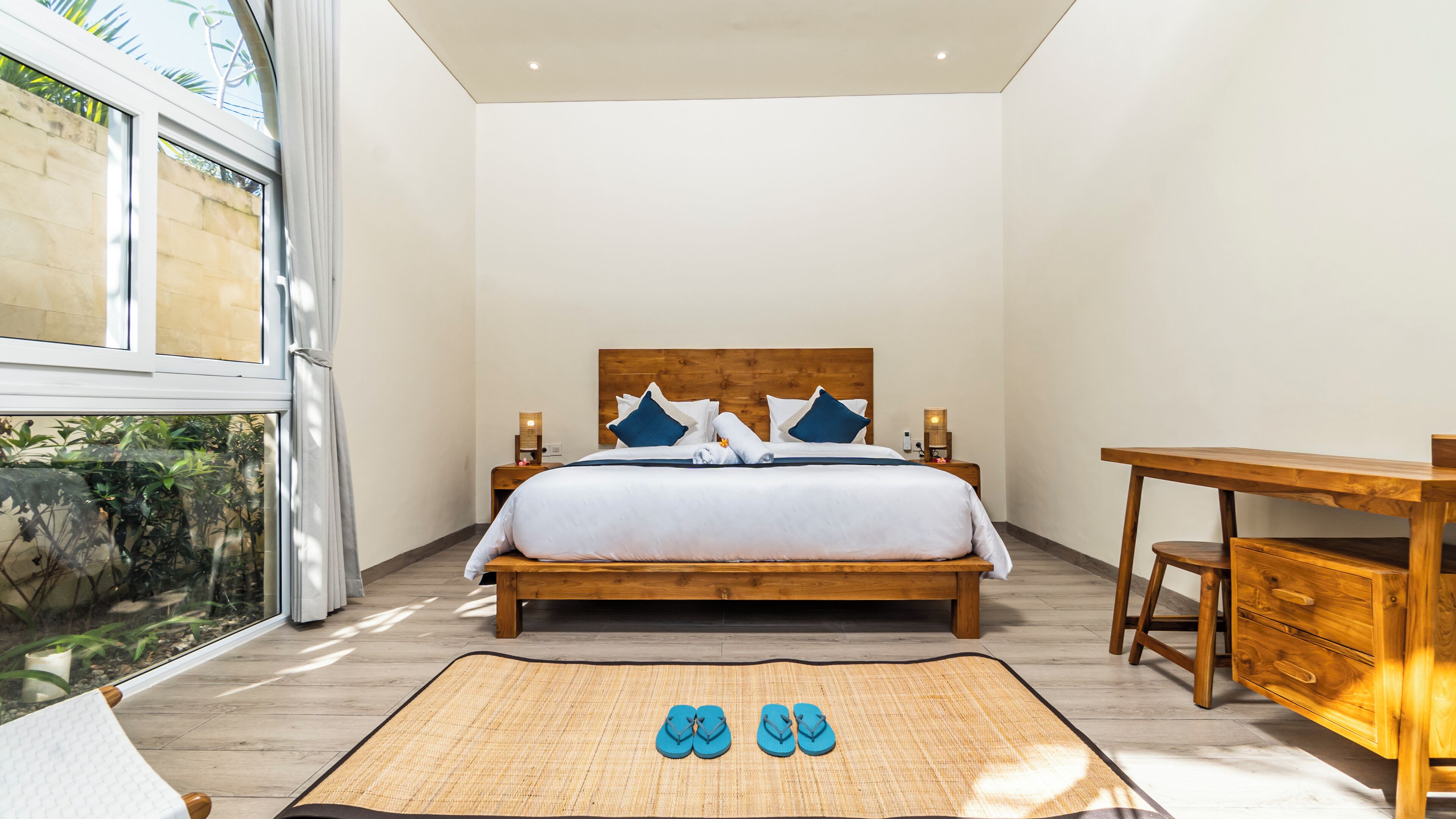 A modern bedroom with a wooden bed, a desk, and a view of greenery outside.