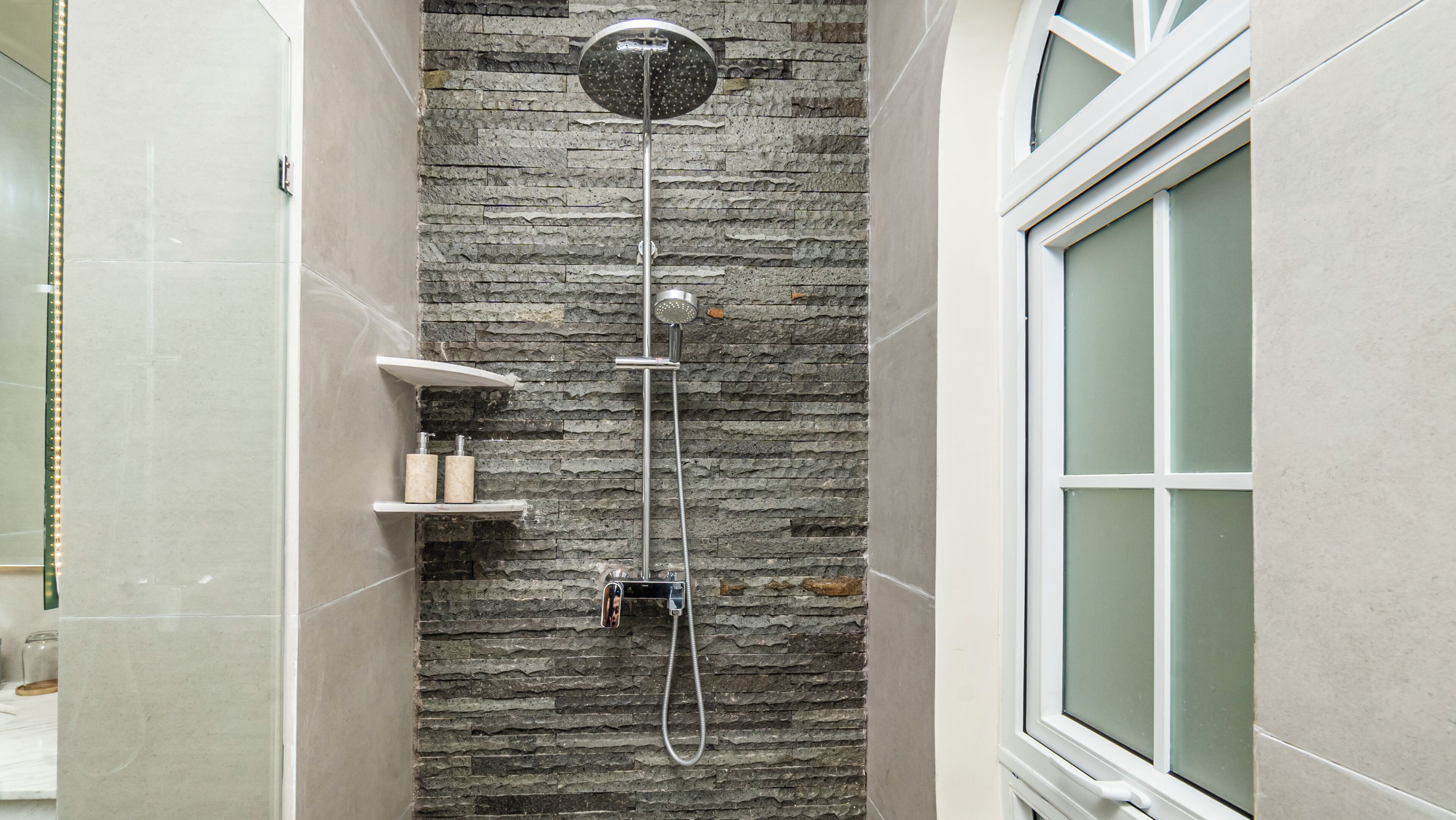 A shower with a stone wall, a handheld showerhead, and a wall-mounted faucet.