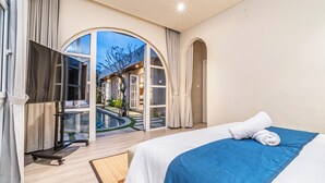 Habitación de hotel moderna con una cama grande, vista a una piscina y un arco abierto que da a un patio.
