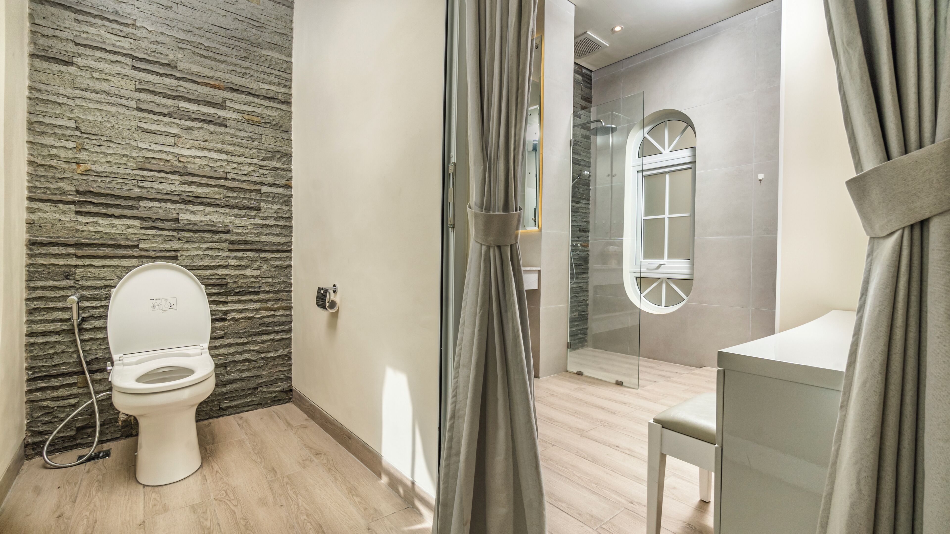 Een badkamer met een stenen muur, toilet, douche met glazen deur en een wastafel met spiegel.