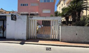 Una entrada protegida con reja metálica, un cartel con la leyenda 'SNAI' y un edificio con balcones al fondo.